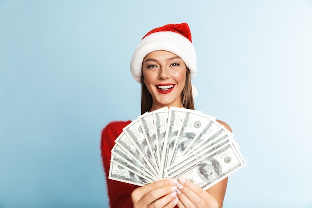 Szczęśliwa młoda kobieta ma na sobie kapelusz Boże Narodzenie, trzymając pieniądze.
