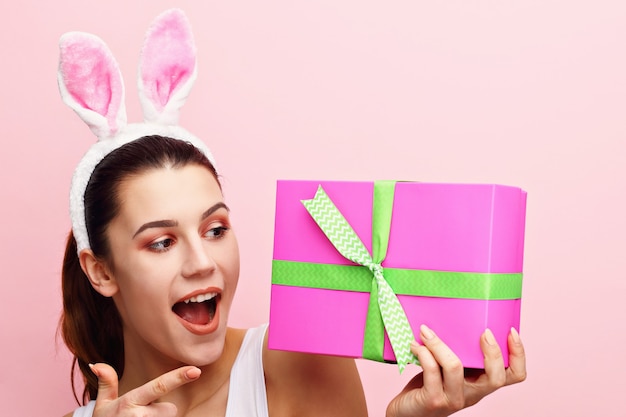 Szczęśliwa młoda kobieta nosi uszy królika i trzyma prezent