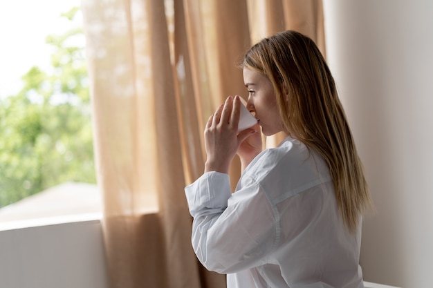 Szczęśliwa młoda kobieta pije herbatę siedząc na krześle w domu. Piękny poranek. Blondynka w białej koszuli mężczyzny