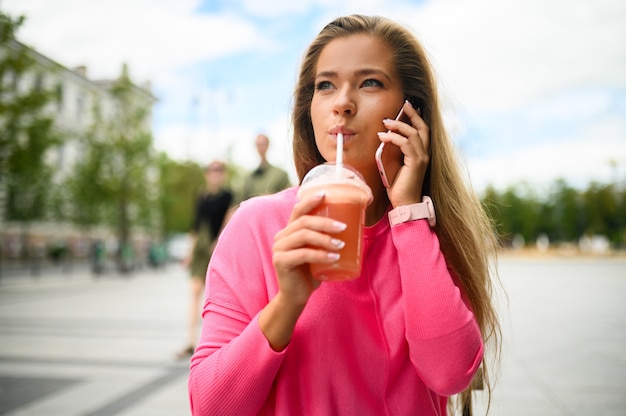 Szczęśliwa młoda kobieta pije kawę na świeżym powietrzu podczas rozmowy przez telefon