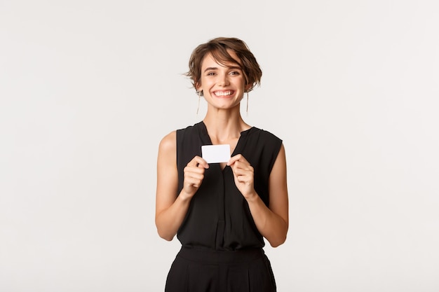 Szczęśliwa młoda kobieta pokazano jej kartę kredytową i uśmiechnięty na białym tle