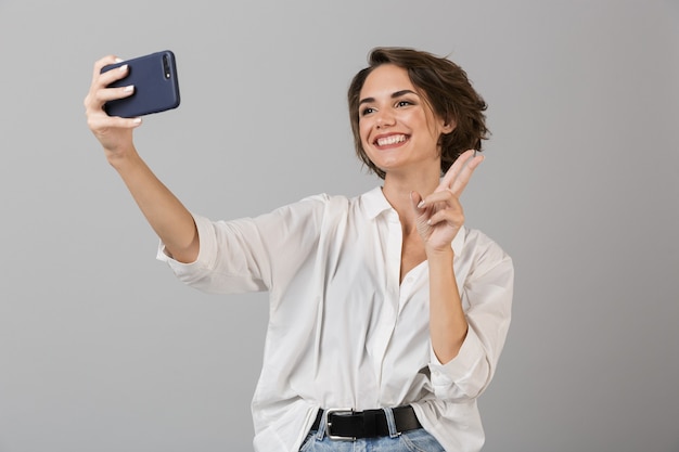 Szczęśliwa Młoda Kobieta Pozowanie Na Białym Tle Nad Szarą ścianą Zrobić Selfie Przez Telefon Komórkowy