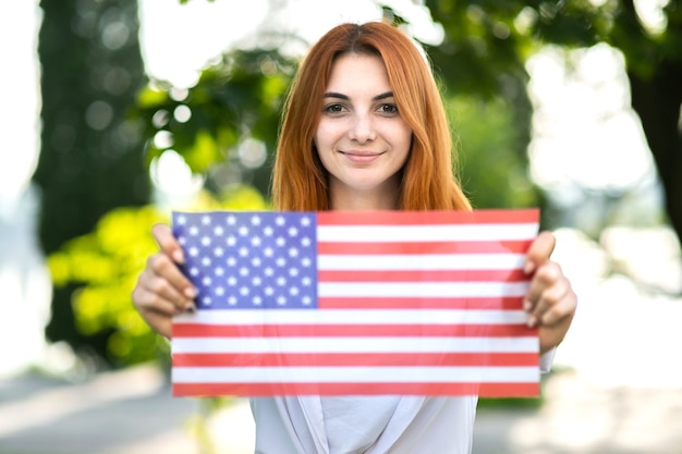 Szczęśliwa młoda kobieta pozuje z narodową flagą USA, trzymając ją w wyciągniętych rękach