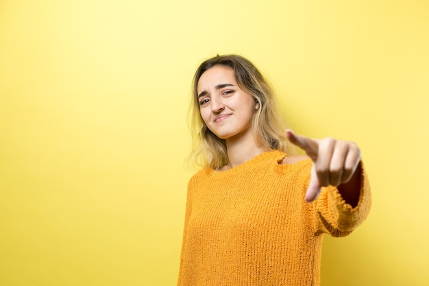 Szczęśliwa młoda kobieta rasy kaukaskiej w pomarańczowym swetrze, wskazując palcami daleko