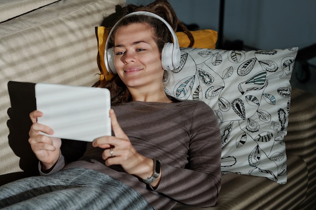 Szczęśliwa Młoda Kobieta Relaks Na Kanapie Podczas Oglądania śmieszne Wideo W Touchpadzie W Ciemnym Pokoju