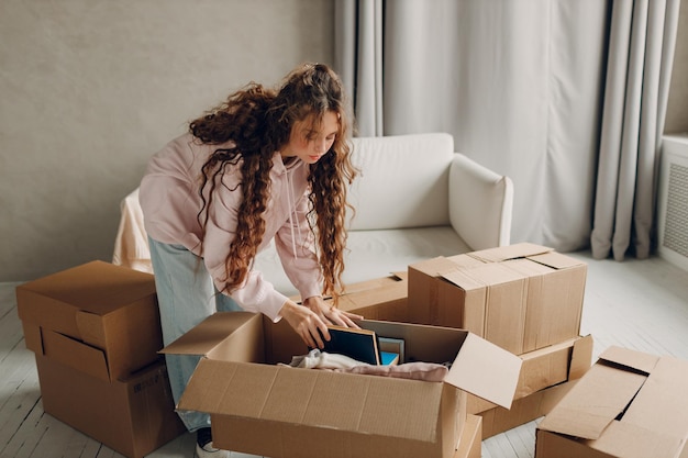 Szczęśliwa młoda kobieta rozpakowuje pudełka z towarami po przeniesieniu kartonowych pudełek do nowego mieszkania