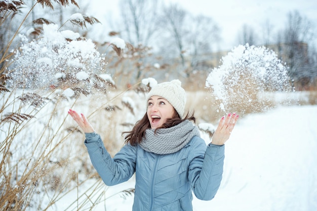 Szczęśliwa młoda kobieta rzuca śniegiem w powietrzu w pogodnym zima dniu