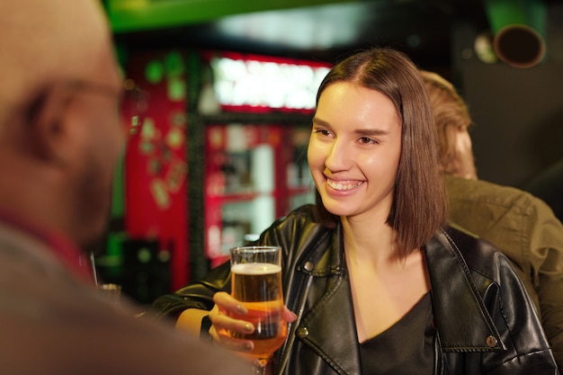 Szczęśliwa młoda kobieta spotykająca się ze swoją przyjaciółką w pubie, pijąca razem piwo i rozmawiająca