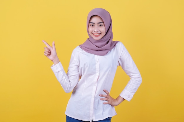 Szczęśliwa młoda kobieta stojąca z palcem wskazującym lewą stronę w hidżabie