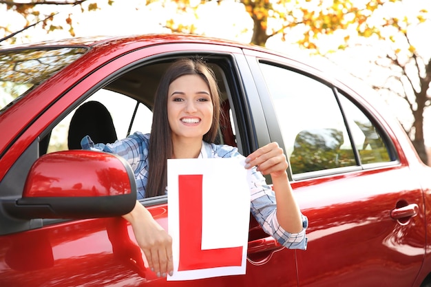 Szczęśliwa młoda kobieta trzyma uczący się kierowca zaloguj się w samochodzie