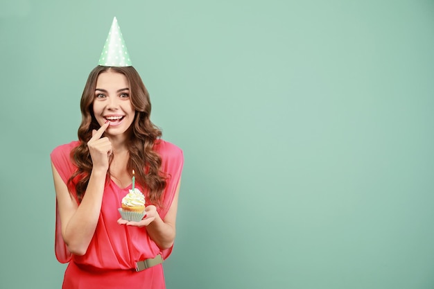 Szczęśliwa młoda kobieta trzyma urodzinową babeczkę ze świecą na kolorowym tle