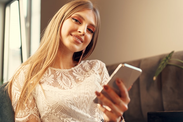 Szczęśliwa młoda kobieta używa jej smartphone podczas gdy siedzący w bufecie