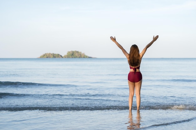 Szczęśliwa młoda kobieta w stroju kąpielowym z podniesionymi rękami na plaży na wyspie Koh Chang Tajlandia