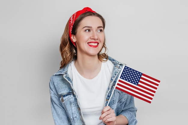 Szczęśliwa Młoda Kobieta Z Czerwoną Szminką Trzyma Małą Amerykańską Flagę I Uśmiecha Się Na Szarym Tle, Dziewczyna Trzyma Flagę Usa, 4 Lipca Dzień Niepodległości, Miejsce Na Kopię