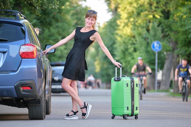 Szczęśliwa młoda kobieta z walizką stojącą w pobliżu jej samochodu podczas podróży samochodem Koncepcja podróży i wakacji