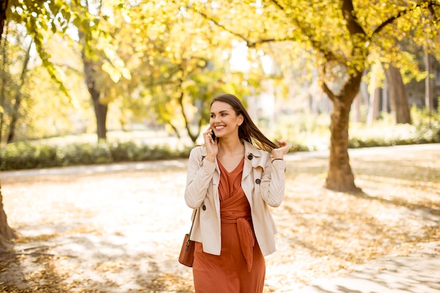 Szczęśliwa młoda kobieta za pomocą telefonu komórkowego w jesiennym parku w piękny dzień