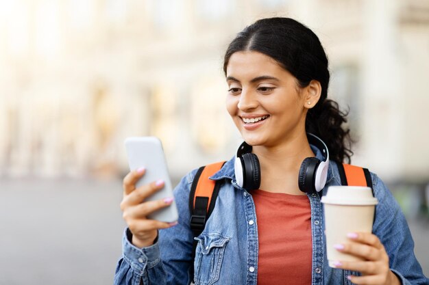 Szczęśliwa młoda kobieta ze wschodu używająca telefonu komórkowego, stojąc na zewnątrz