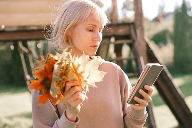 Szczęśliwa młoda ładna kobieta spacerująca na świeżym powietrzu w jesiennym parku za pomocą telefonu komórkowego na czacie