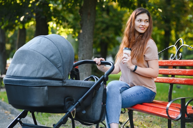 Szczęśliwa młoda matka z dzieckiem w wózku siedzącym na ławce w jesiennym parku