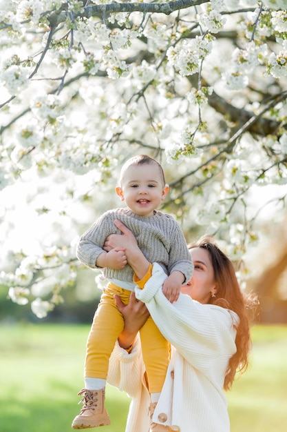 Szczęśliwa młoda matka z małym synkiem spaceruje po kwitnącym ogrodzie Mama z 1-letnim dzieckiem Wiosna
