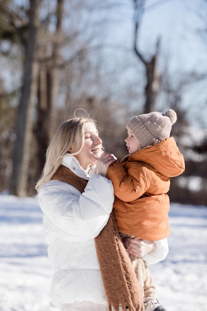Szczęśliwa młoda matka z synem spacerują w zimowym parku Portret szczęśliwej rodziny na świeżym powietrzu Chłopiec rzucający śnieg w matkę