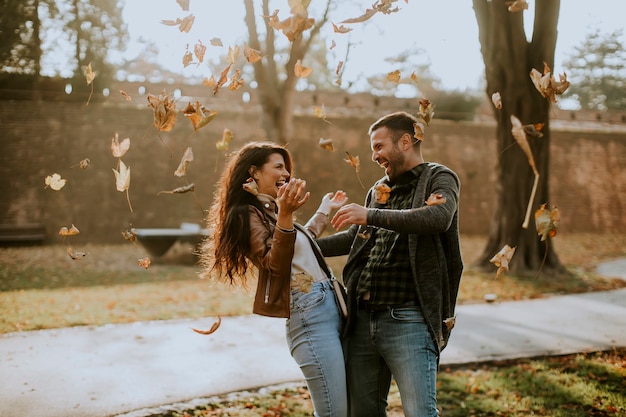 Szczęśliwa młoda para bawi się jesiennymi liśćmi w parku