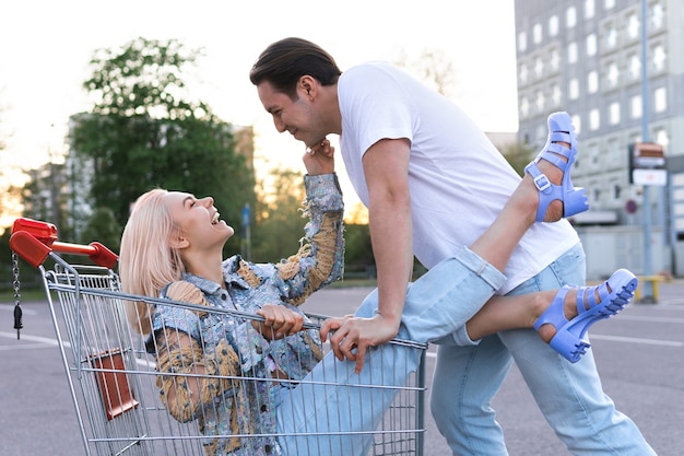 Zdjęcie szczęśliwa młoda para bawi się wózkiem na zakupy na parkingu supermarketu