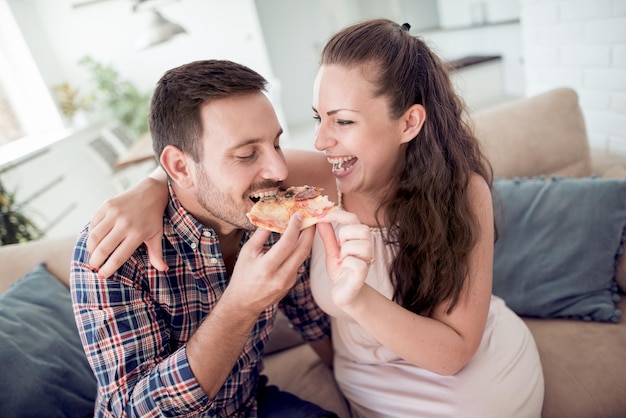 Szczęśliwa młoda para jedząca pizzę w salonie