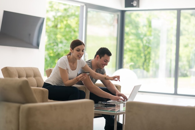 szczęśliwa młoda para kupująca online za pomocą laptopa, komputera i karty kredytowej w swojej luksusowej willi