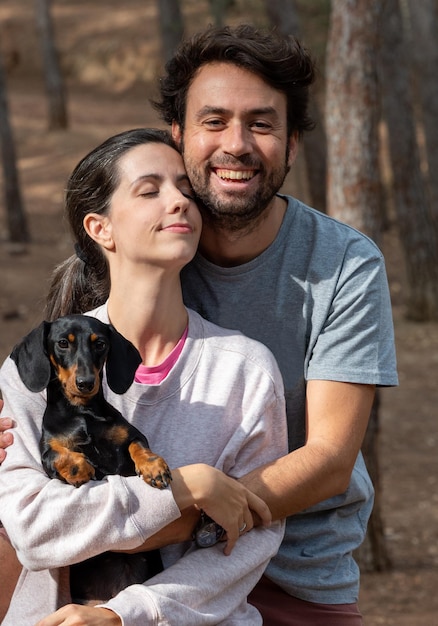 Szczęśliwa młoda para rasy kaukaskiej uśmiecha się z psem miniaturowym jamnikiem w lesie