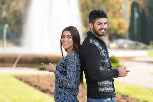 Szczęśliwa młoda para stojąca na zewnątrz i korzystająca ze smartfona