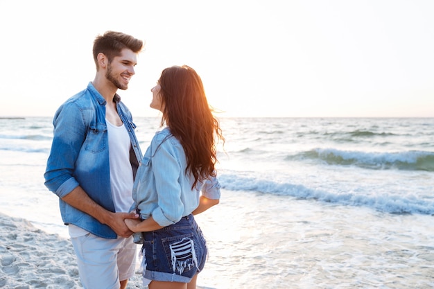 Szczęśliwa młoda para trzymając się za ręce i patrząc na siebie na plaży