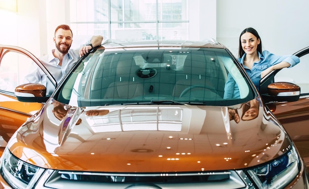 Szczęśliwa młoda para wybiera i kupuje nowy samochód dla rodziny w salonie