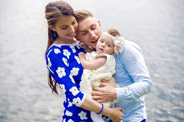 Szczęśliwa młoda para z córeczką stojącą w wodzie dziewczyna w niebieskiej sukience, koszula chłopca w stylu marynistycznym