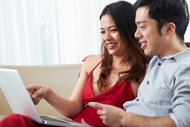 Szczęśliwa młoda para z laptopem i kartą kredytową dyskutująca o tym, co kupić na dużej wyprzedaży w sklepie internetowym