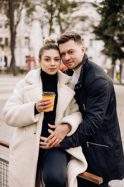 Szczęśliwa młoda para zakochanych w odzieży wierzchniej spacerująca po ulicy i pijąca kawę Rekreacja na świeżym powietrzu Młode małżeństwo