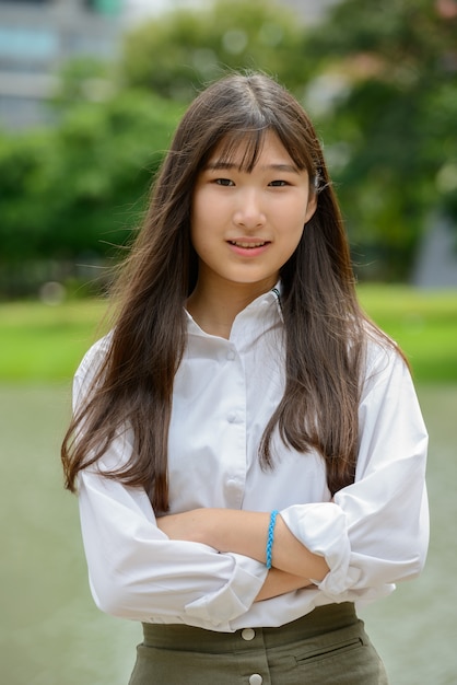Szczęśliwa młoda piękna Azjatycka nastoletnia kobieta z rękami krzyżował przy parkiem