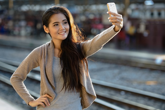 Szczęśliwa młoda piękna kobieta Azji biorąc selfie na stacji kolejowej
