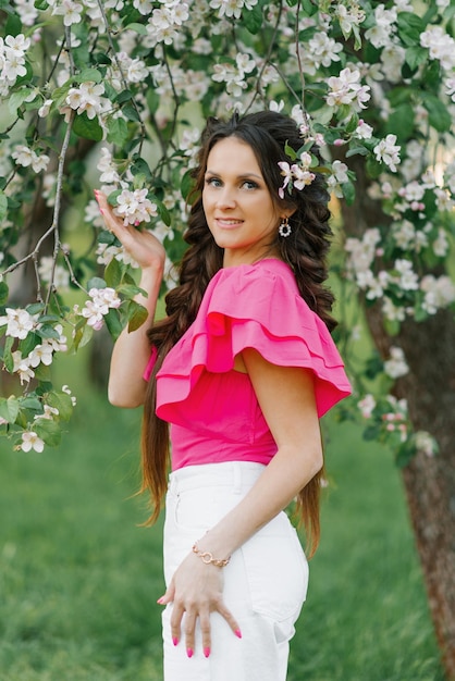 Szczęśliwa młoda piękna kobieta w wiosennym ogrodzie trzymająca gałązkę kwitnących jabłoni i uśmiechnięta