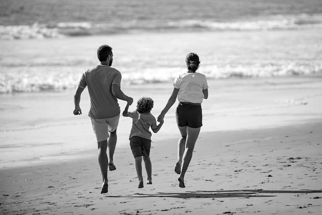 Szczęśliwa młoda rodzina biega i skacze na letniej plaży koncepcja rodzinnych zajęć rekreacyjnych dziecko z rodzicami