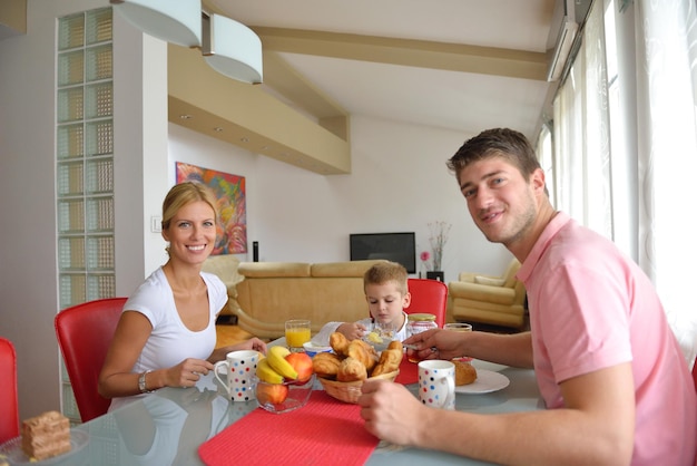 szczęśliwa młoda rodzina je zdrowe śniadanie w kuchni z czerwonymi detalami na jasnym świetle poranka