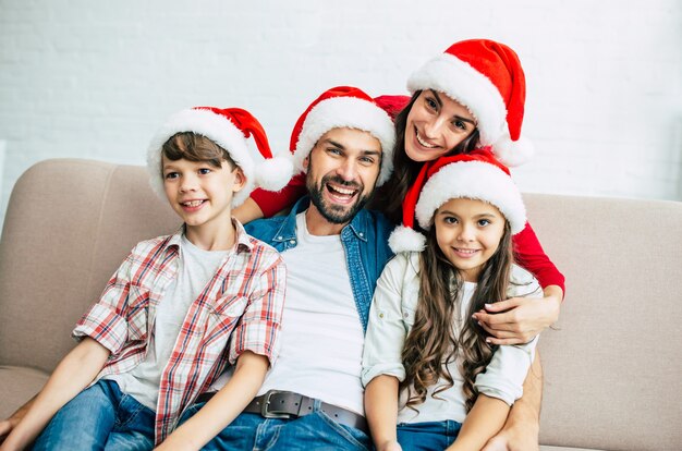 Szczęśliwa młoda rodzina spędza czas w salonie w czerwonych kapeluszach Santa