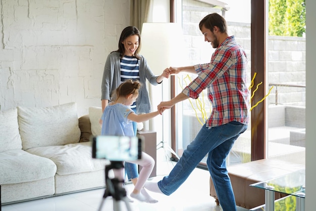 Szczęśliwa młoda rodzina tańczy w domu ze swoją małą uroczą córką, kręci wideo.