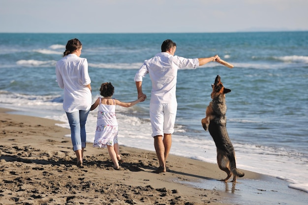 szczęśliwa młoda rodzina w białych ubraniach bawi się i bawi z pięknym psem na wakacjach na pięknej plaży