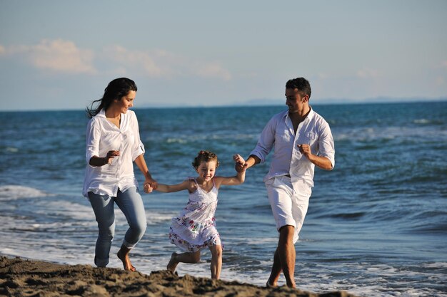 szczęśliwa młoda rodzina w białych ubraniach bawi się na wakacjach na pięknej plaży
