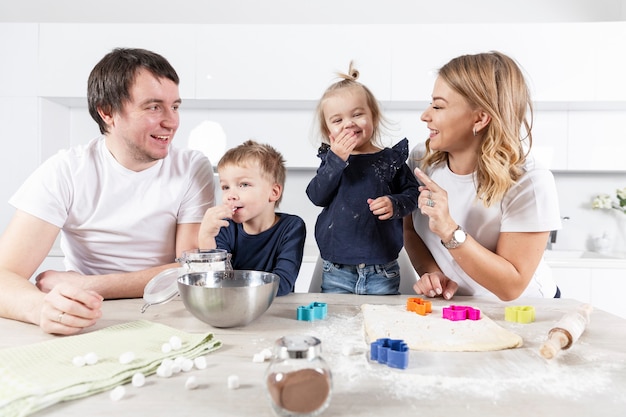 Szczęśliwa młoda rodzina z dwójką małych dzieci radośnie przygotowuje ciasteczka ciasta w kuchni. Miłość i czułość w związku.