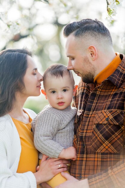 Szczęśliwa młoda rodzina z małym synkiem spaceruje po kwitnącym ogrodzie Mama i tata z 1-letnim dzieckiem Wiosna