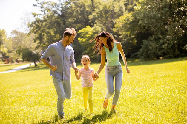 Szczęśliwa młoda rodzina z uroczą małą córeczką bawiącą się w parku w słoneczny dzień