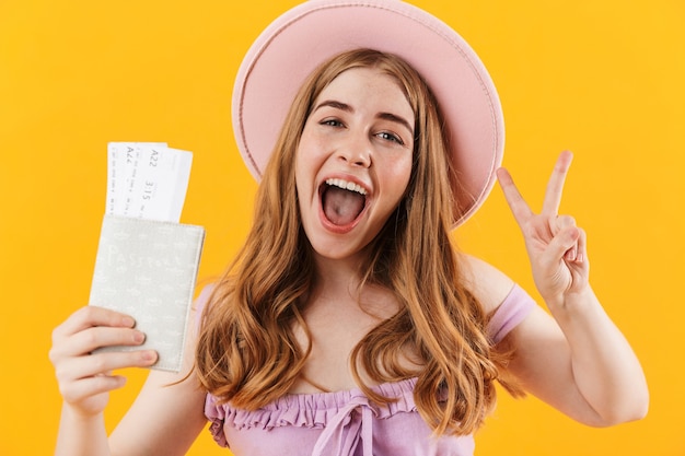 Zdjęcie szczęśliwa młoda śliczna nastolatka pozuje na białym tle nad żółtą ścianą, trzymając bilety i paszport pokazujący pokój.