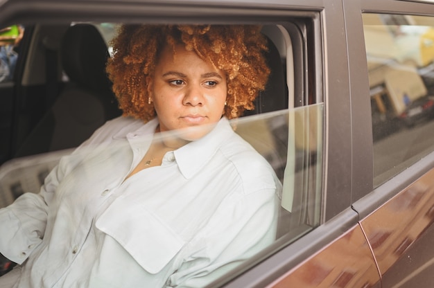 Szczęśliwa młoda uśmiechnięta afroamerykanka czerwony afrowłosy kierowca siedzący w nowym brązowym samochodzie uśmiechnięty